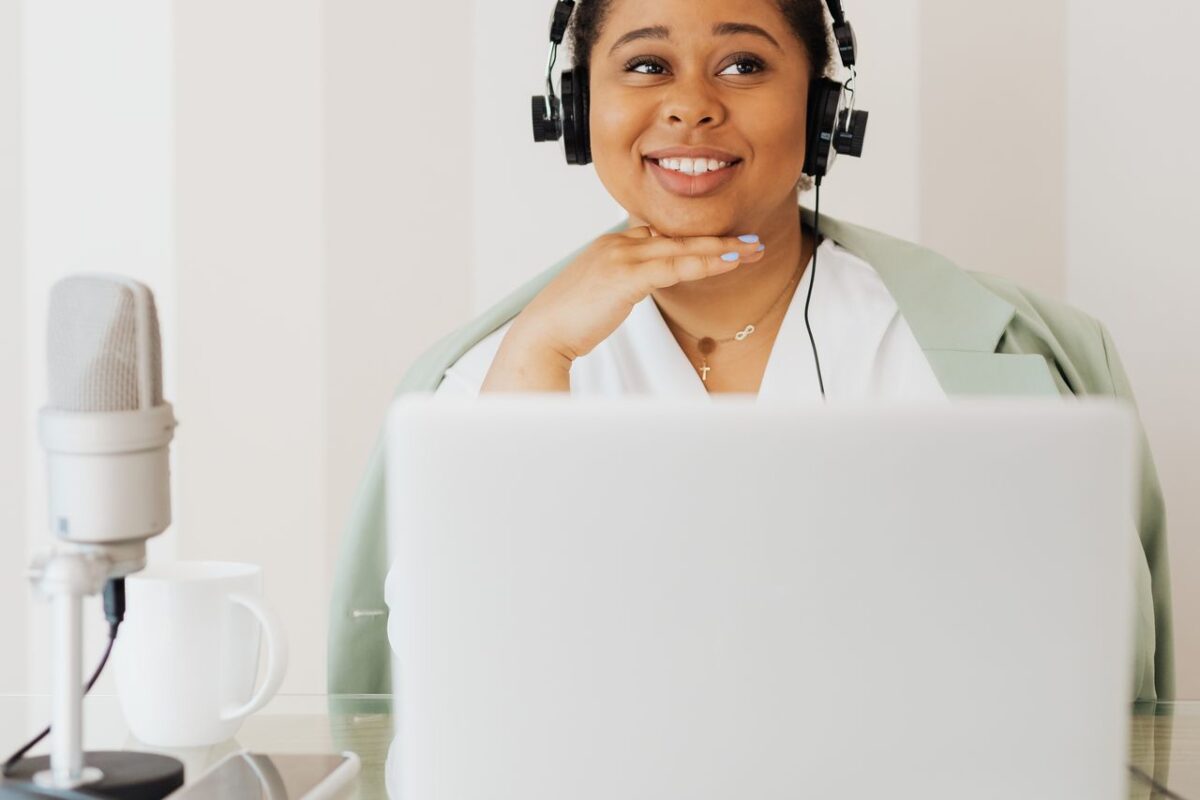 À propos A woman smiling while podcasting at home, wearing headphones and using a microphone.